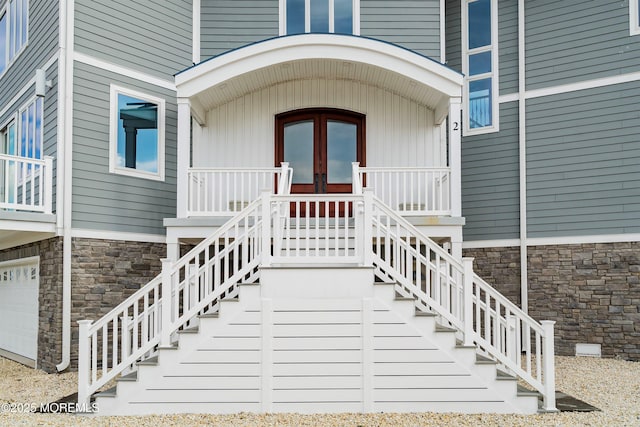 doorway to property with covered porch, french doors, and a garage