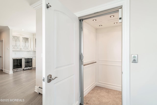 interior space with hardwood / wood-style floors, beverage cooler, elevator, baseboard heating, and decorative backsplash