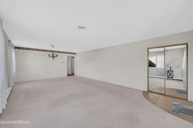 empty room featuring light tile patterned flooring, visible vents, a chandelier, and light colored carpet