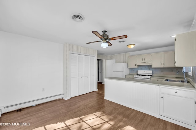 kitchen with light countertops, baseboard heating, a sink, wood finished floors, and white appliances