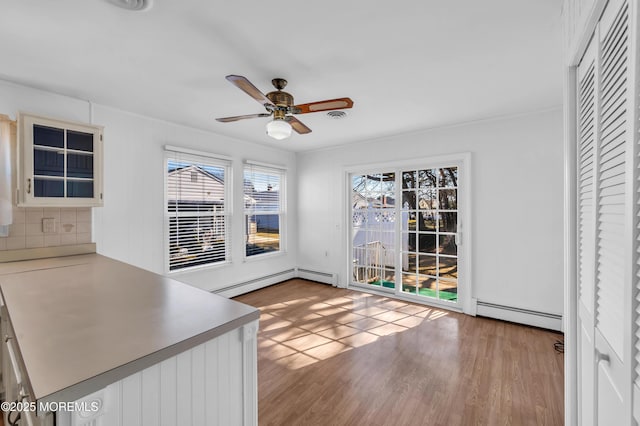 unfurnished dining area with a baseboard heating unit, ceiling fan, and light wood finished floors