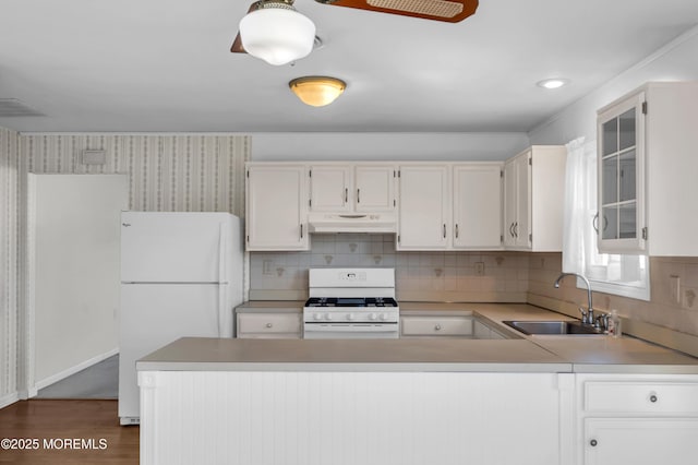 kitchen featuring white appliances, glass insert cabinets, under cabinet range hood, white cabinetry, and a sink