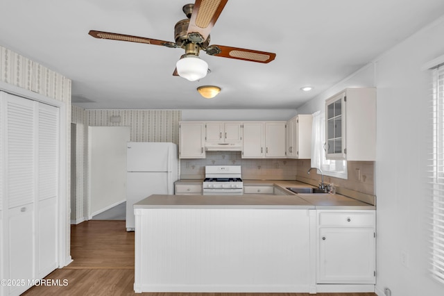 kitchen featuring white appliances, white cabinets, glass insert cabinets, light countertops, and a sink