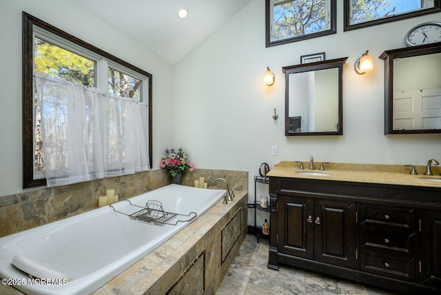 bathroom with lofted ceiling, tiled bath, and vanity