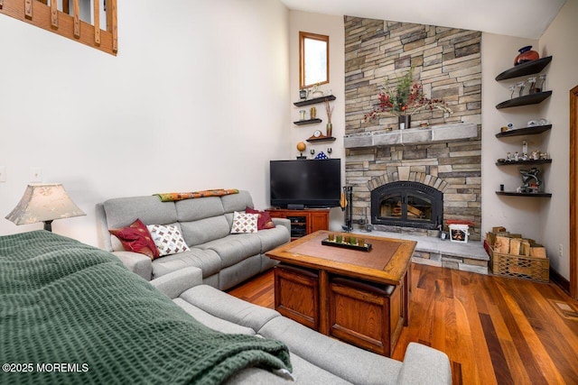 living area with vaulted ceiling, a stone fireplace, and wood finished floors