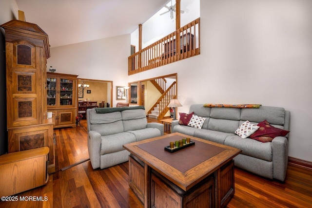 living room with a ceiling fan, a high ceiling, stairway, and dark wood-type flooring