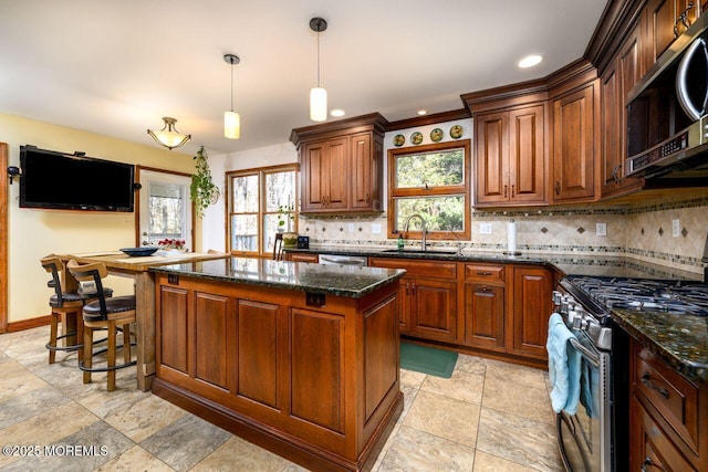 kitchen featuring decorative light fixtures, appliances with stainless steel finishes, a kitchen island, a sink, and dark stone countertops