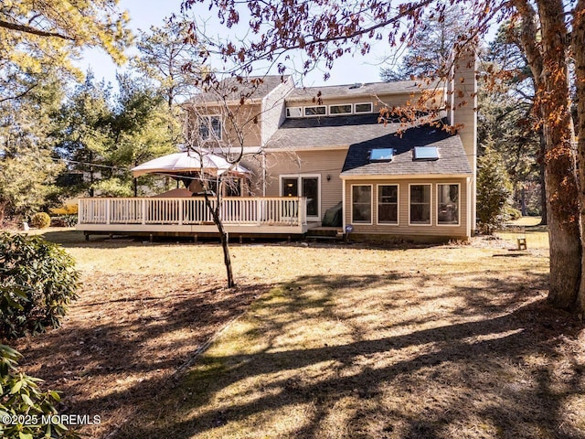 back of property with a chimney, a deck, a lawn, and a gazebo