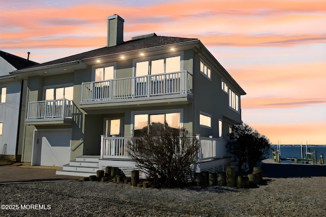 back of property at dusk with a balcony, a garage, and a chimney