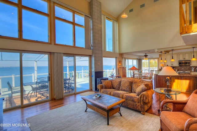 living room featuring a water view, visible vents, a ceiling fan, high vaulted ceiling, and light wood-type flooring