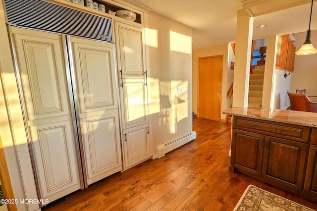 kitchen with light stone counters, wood finished floors, cream cabinets, baseboard heating, and a textured ceiling