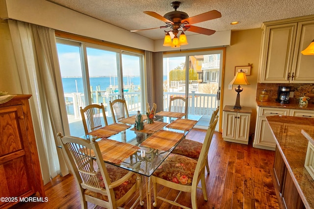 dining room featuring dark wood-style floors, a water view, a textured ceiling, and a ceiling fan