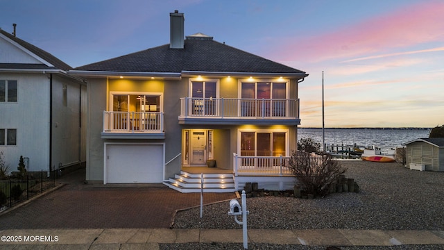 view of front of property featuring a balcony, a chimney, a water view, an attached garage, and decorative driveway