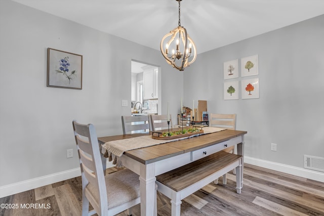 dining space with sink, a notable chandelier, and light hardwood / wood-style flooring