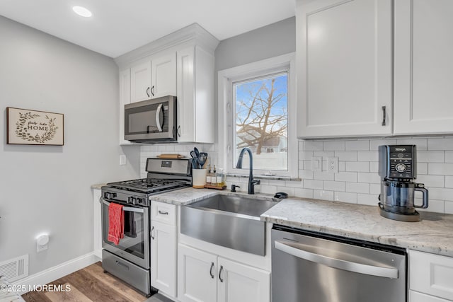 kitchen with sink, light stone counters, light wood-type flooring, white cabinetry, and stainless steel appliances