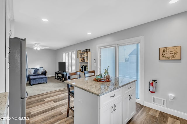 kitchen featuring a kitchen island, stainless steel refrigerator, white cabinets, and light stone countertops