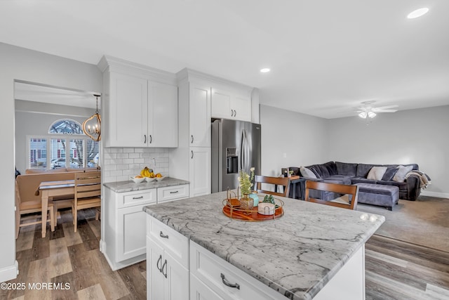 kitchen featuring white cabinetry, a kitchen island, light stone countertops, and stainless steel fridge with ice dispenser