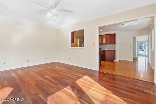 unfurnished living room featuring dark wood-style floors, baseboards, and a ceiling fan