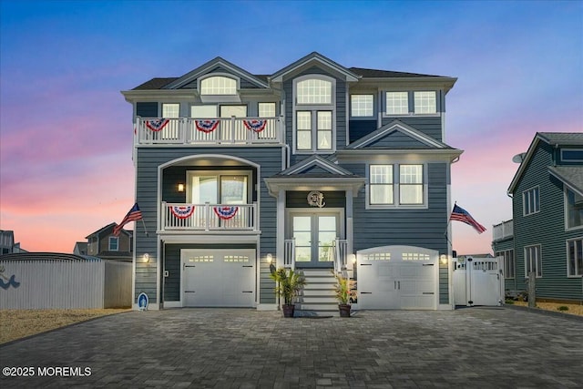 view of front of house featuring decorative driveway, french doors, an attached garage, fence, and a balcony