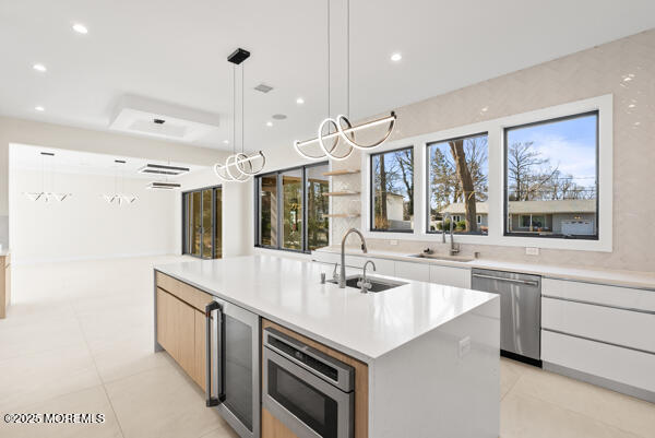 kitchen with hanging light fixtures, stainless steel appliances, an island with sink, white cabinets, and sink