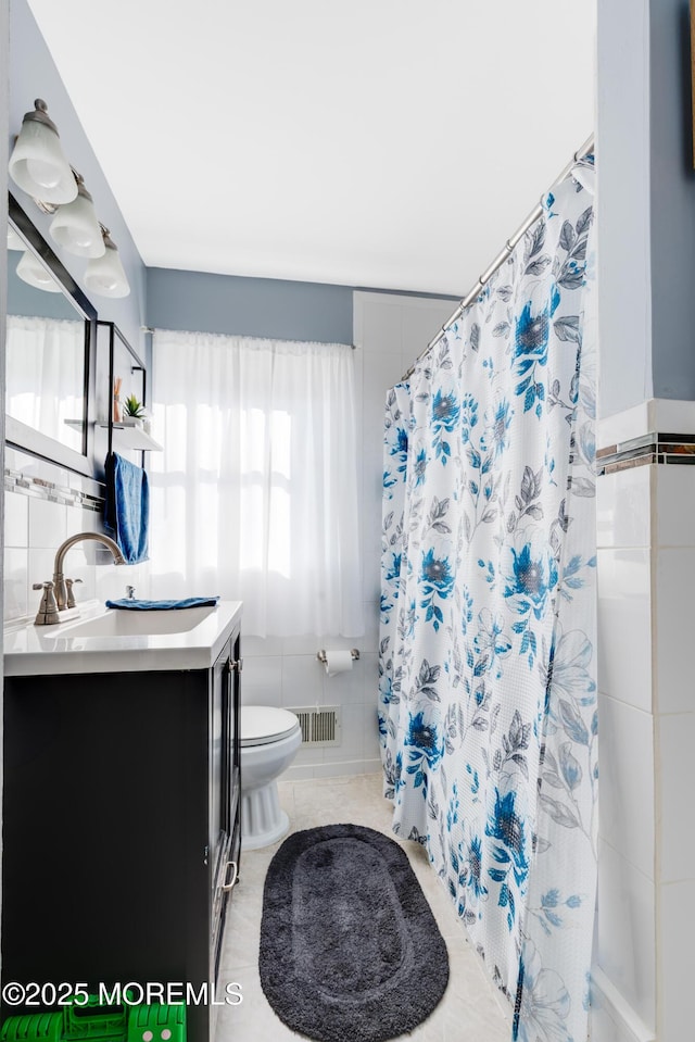 bathroom with curtained shower, vanity, tile walls, tile patterned flooring, and toilet