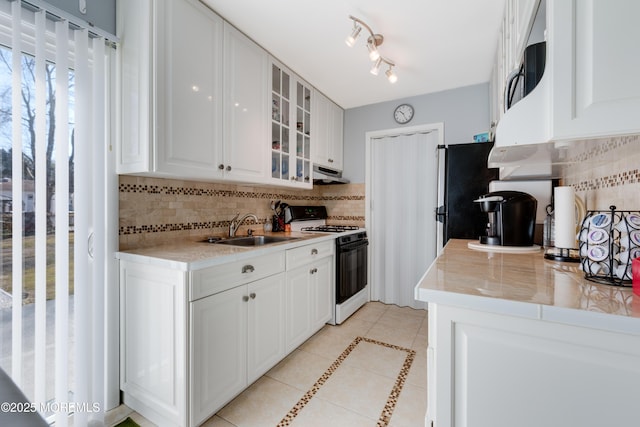 kitchen featuring gas stove, backsplash, light tile patterned floors, sink, and white cabinetry