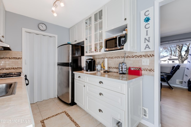 kitchen with stainless steel appliances, sink, backsplash, light tile patterned floors, and white cabinets