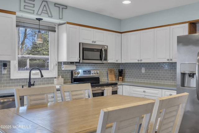 kitchen with tasteful backsplash, appliances with stainless steel finishes, pendant lighting, and white cabinets