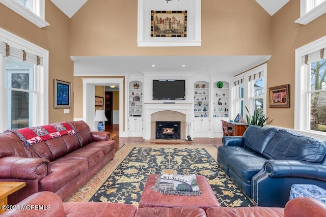 living area featuring high vaulted ceiling, a fireplace, wood finished floors, and built in features