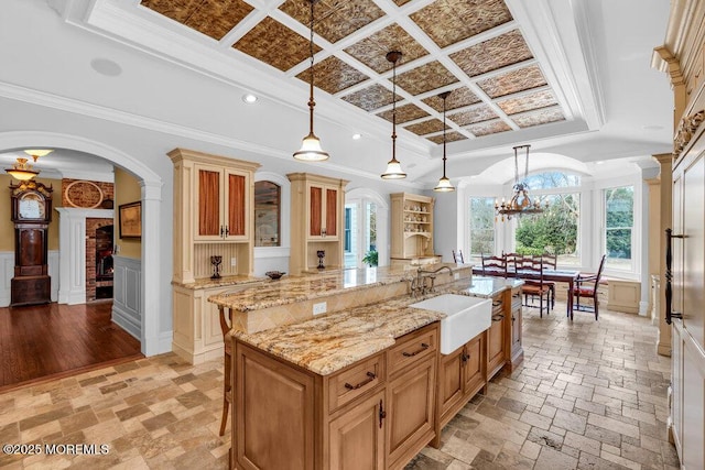 kitchen with pendant lighting, crown molding, a large island, glass insert cabinets, and a sink