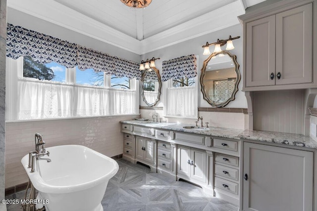 full bath with double vanity, a soaking tub, a sink, and tile walls