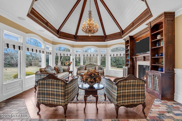 sunroom with a healthy amount of sunlight, a warm lit fireplace, vaulted ceiling, and an inviting chandelier