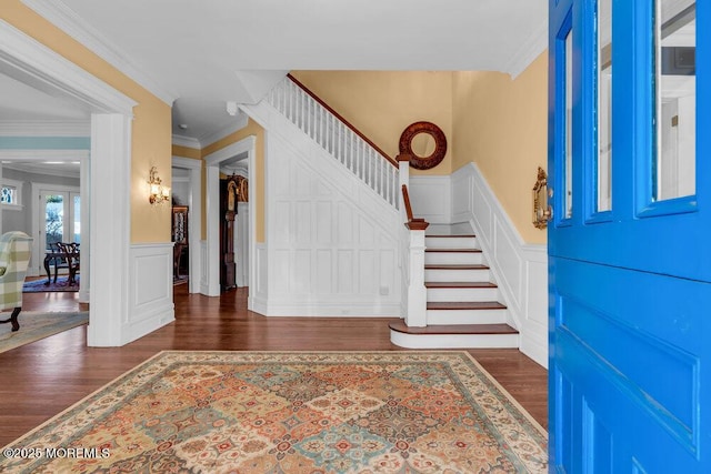 entryway with ornamental molding, dark wood finished floors, a decorative wall, and stairs