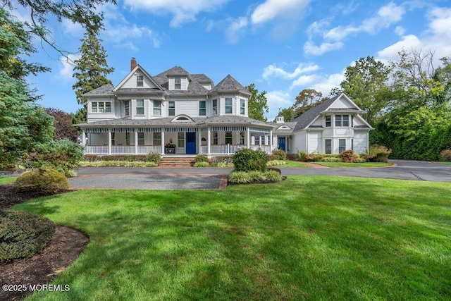 victorian-style house featuring aphalt driveway, a chimney, a front lawn, and a porch