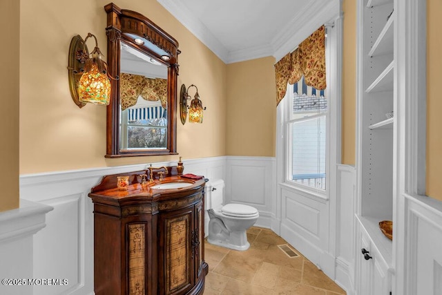 half bath with toilet, a wainscoted wall, visible vents, and crown molding