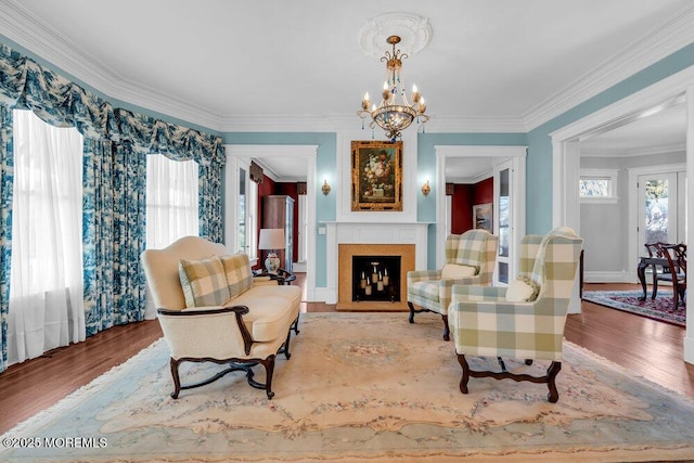 living area featuring ornamental molding, a fireplace, wood finished floors, and a notable chandelier