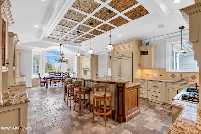 kitchen featuring cream cabinets, paneled refrigerator, a center island with sink, and pendant lighting