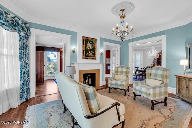 living area with a fireplace, a chandelier, wood finished floors, and ornamental molding