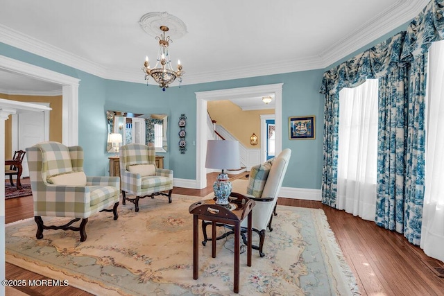 living area with wood finished floors, baseboards, stairs, ornamental molding, and an inviting chandelier