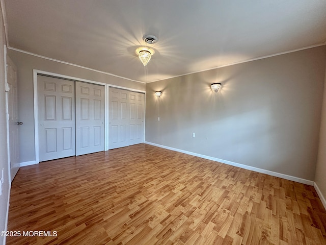 unfurnished bedroom with crown molding, light wood-style flooring, baseboards, and two closets