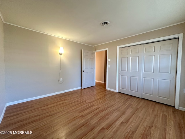 unfurnished bedroom with a closet, visible vents, light wood-style floors, ornamental molding, and baseboards