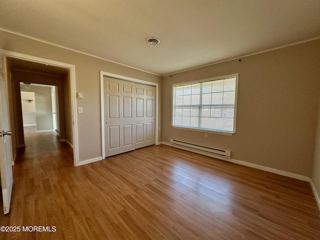 unfurnished bedroom featuring baseboards, visible vents, wood finished floors, a baseboard heating unit, and a closet