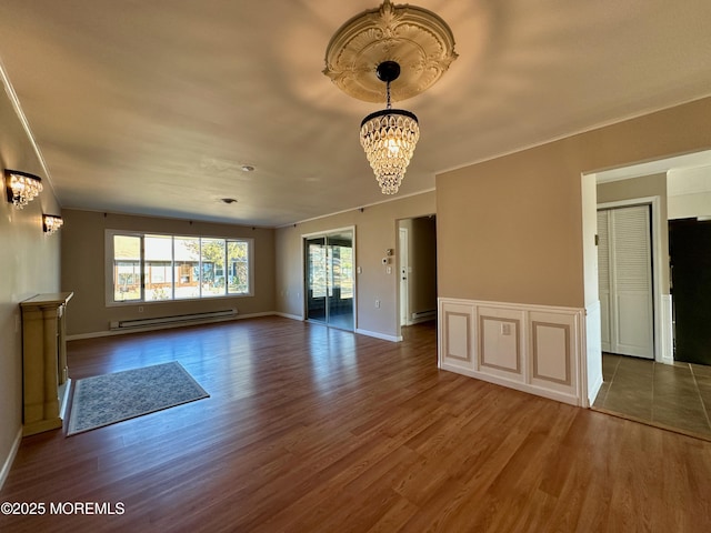 unfurnished room with a baseboard radiator, crown molding, a notable chandelier, and wood finished floors