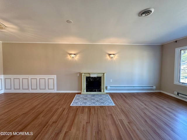 unfurnished living room with a baseboard heating unit, a high end fireplace, visible vents, and wood finished floors