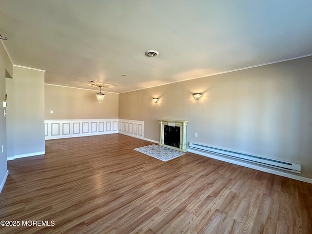 unfurnished living room featuring visible vents, a premium fireplace, a baseboard heating unit, and wood finished floors