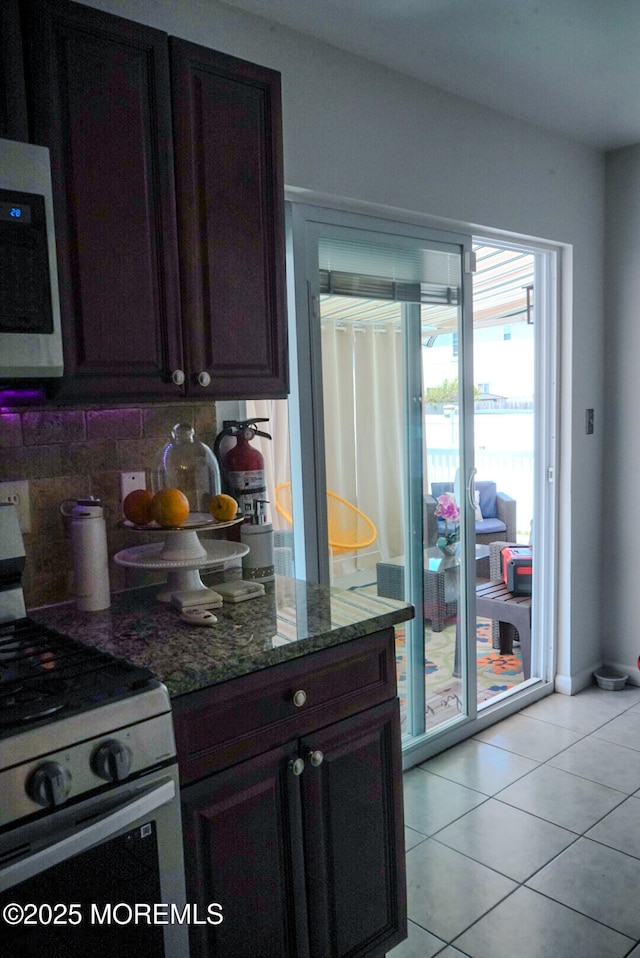 kitchen with light tile patterned flooring, tasteful backsplash, dark stone counters, and range with gas cooktop