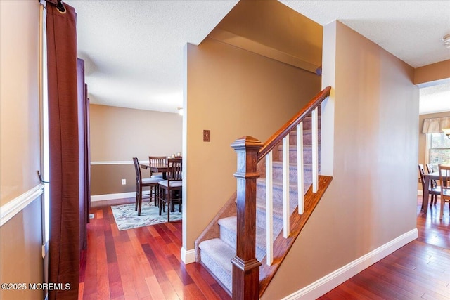 stairs featuring a textured ceiling, hardwood / wood-style flooring, and baseboards