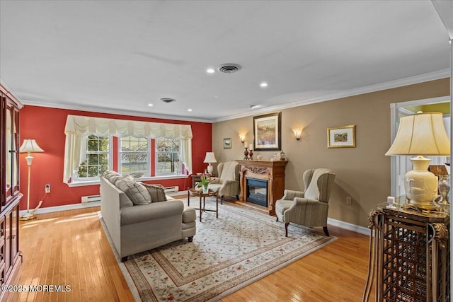 living area with ornamental molding, a glass covered fireplace, visible vents, and light wood-style flooring