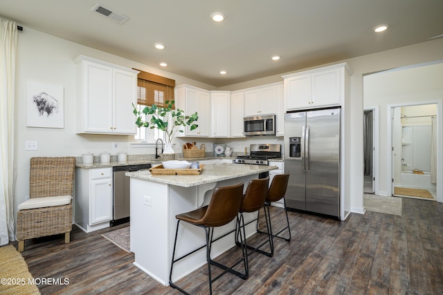 kitchen featuring dark wood-style floors, a center island, stainless steel appliances, visible vents, and white cabinetry