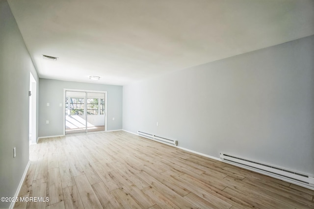 spare room featuring a baseboard heating unit, baseboards, visible vents, and wood finished floors